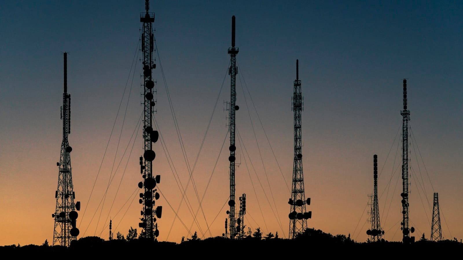 A row of cell-tower silhouettes against a deep orange sunset — the unreliable mobile infrastructure our engine has to absorb.